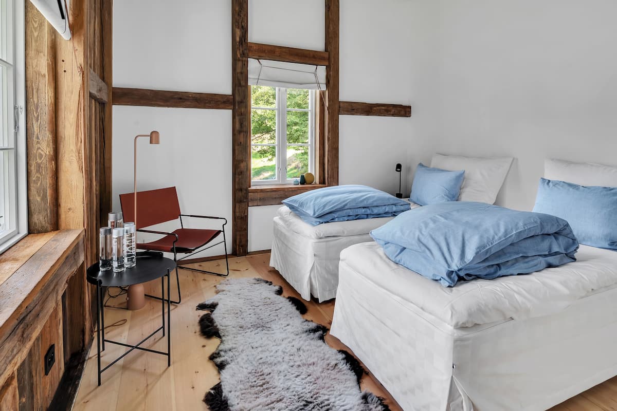 A bedroom with two beds, a wooden chair, a table with water bottles, and a window with a view.