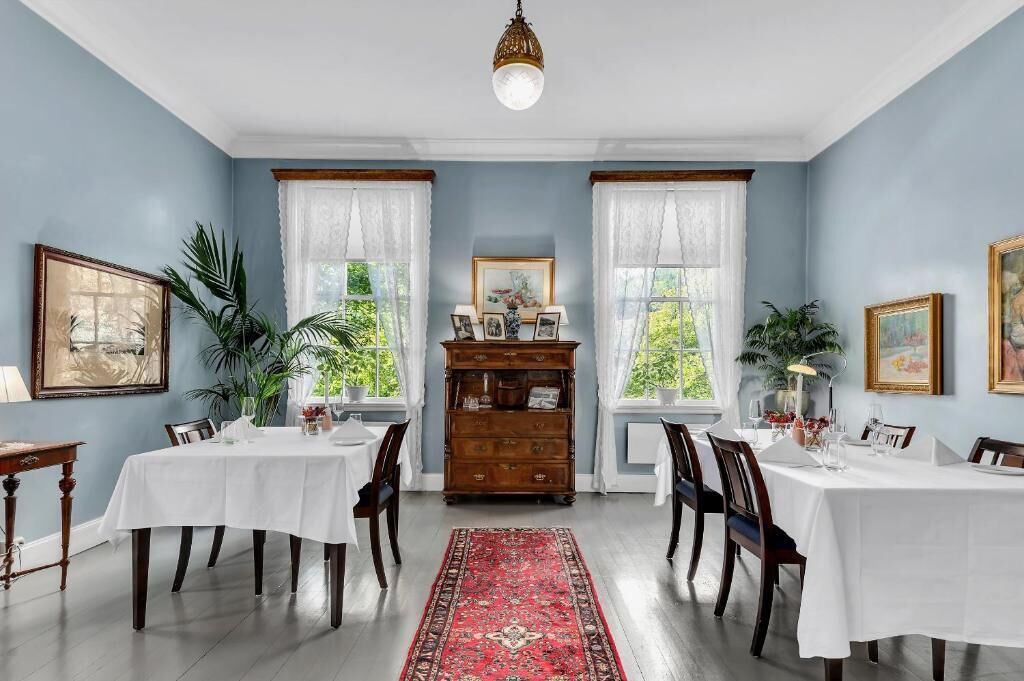 A dining room with two tables set for six, a red rug, and a wooden cabinet with framed pictures.