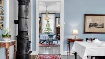 A hallway with a large black stove, a dining area with blue chairs, a chandelier, and a framed picture on the wall.