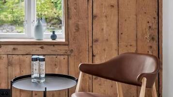 Un intérieur en bois, avec un fauteuil en cuir, une petite table ronde agrémentée de salières et une fenêtre donnant sur un paysage verdoyant.