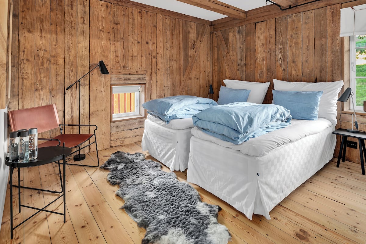 A wooden-paneled room with two beds, a chair, a table, and a fur rug.