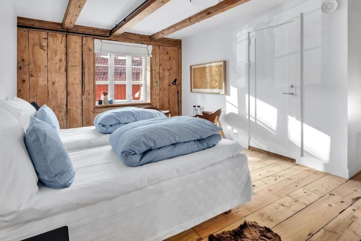 A bedroom with a wooden ceiling, a large window, and a white door.