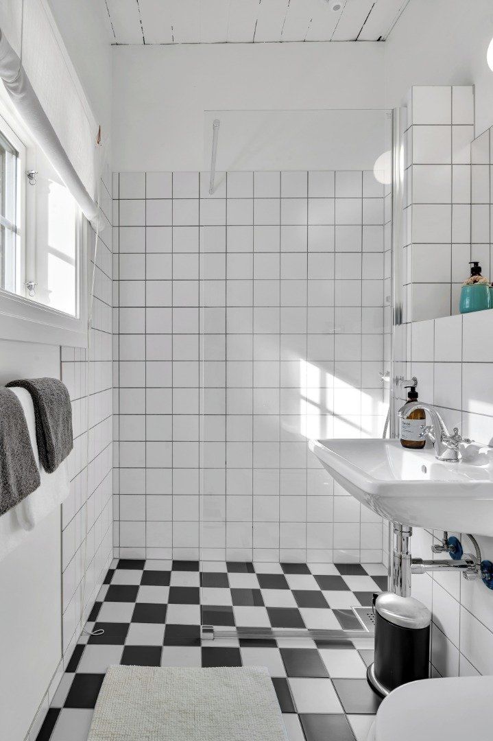 A bathroom with white tiled walls and floor, a checkered floor pattern, a white sink, a mirror, and a window.