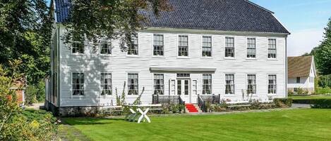 A large, white, two-story house with a dark roof, surrounded by a well-maintained lawn and garden.