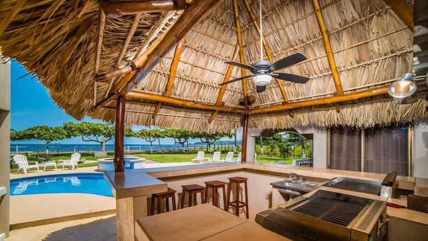 Un área de bar al aire libre con piscina, sillas de descanso y techo de paja.