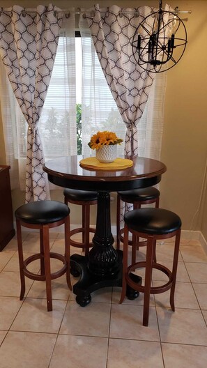 Une table de salle à manger ronde, accompagnée de trois tabourets, un vase rempli de fleurs et un lustre.