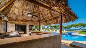 Un bar junto a la piscina con techo de paja, asientos al aire libre y vista al océano.