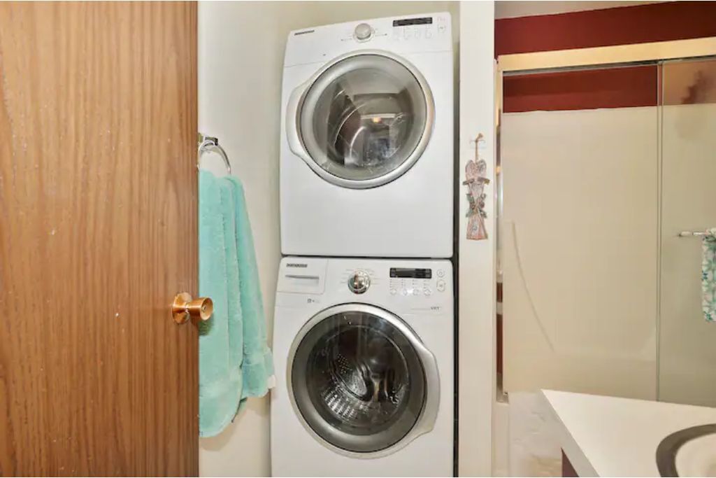 Un lavadero con dos lavadoras superpuestas y una puerta de madera.