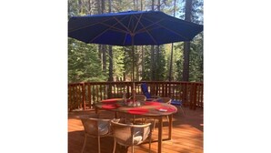 A wooden deck with a table and chairs, an umbrella, and a railing. - Daquino Tahoe Donner Retreat - Pet Friendly! (Truckee)