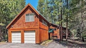 A wooden cabin with a garage, surrounded by trees. - Daquino Tahoe Donner Retreat - Pet Friendly! (Truckee)