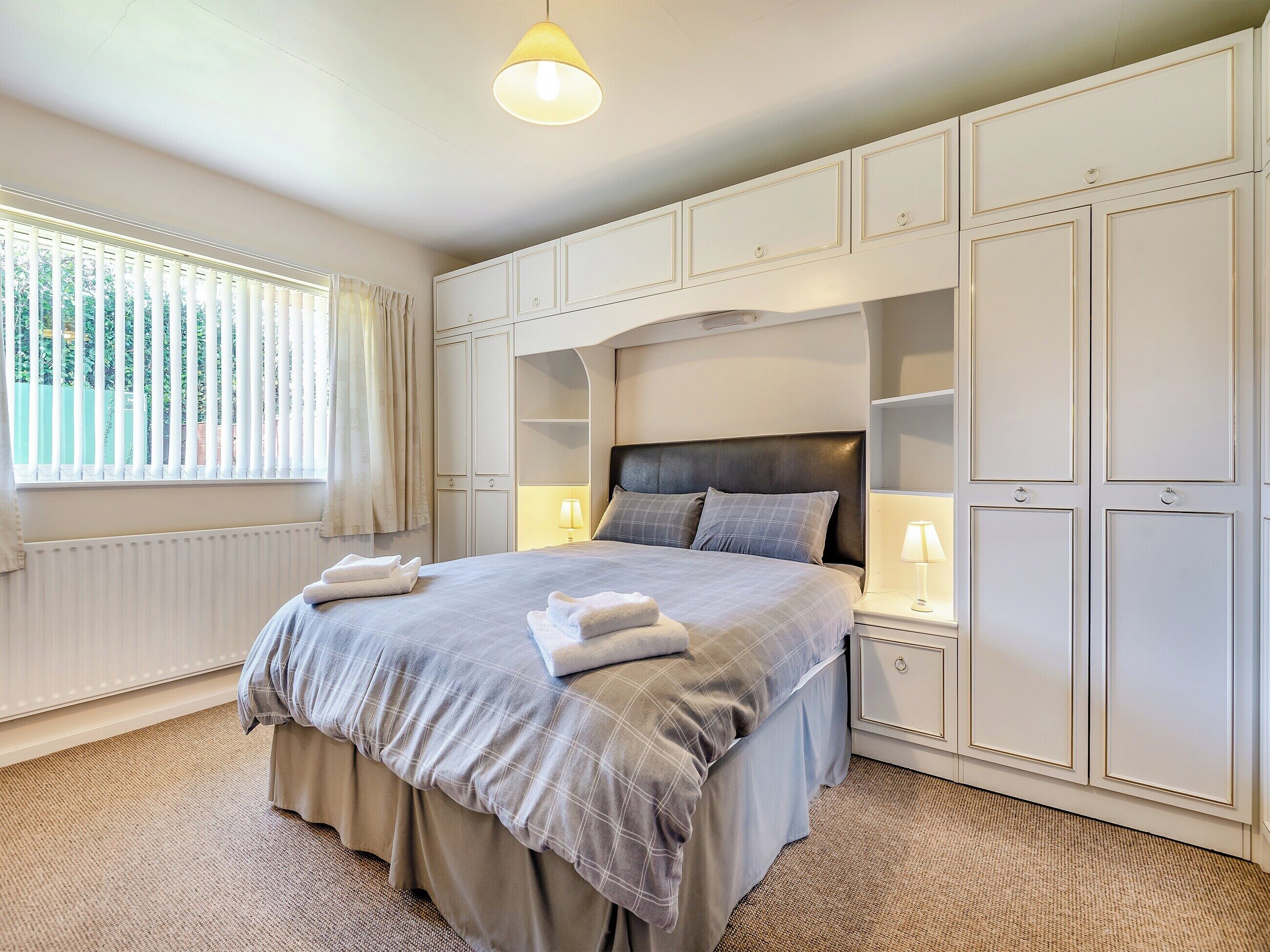 A neatly arranged bedroom with a large bed, bedside lamps, and built-in wardrobes.