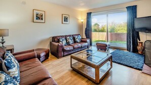 A living room with a brown leather sofa, a glass coffee table, and a large sliding glass door leading to a backyard. - 5 bedroom accommodation in Heritage Marina, near Congleton (Heritage Marina, near Congleton)