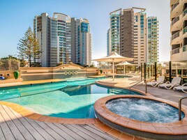 A swimming pool with a hot tub, lounge chairs, and a wooden deck.
