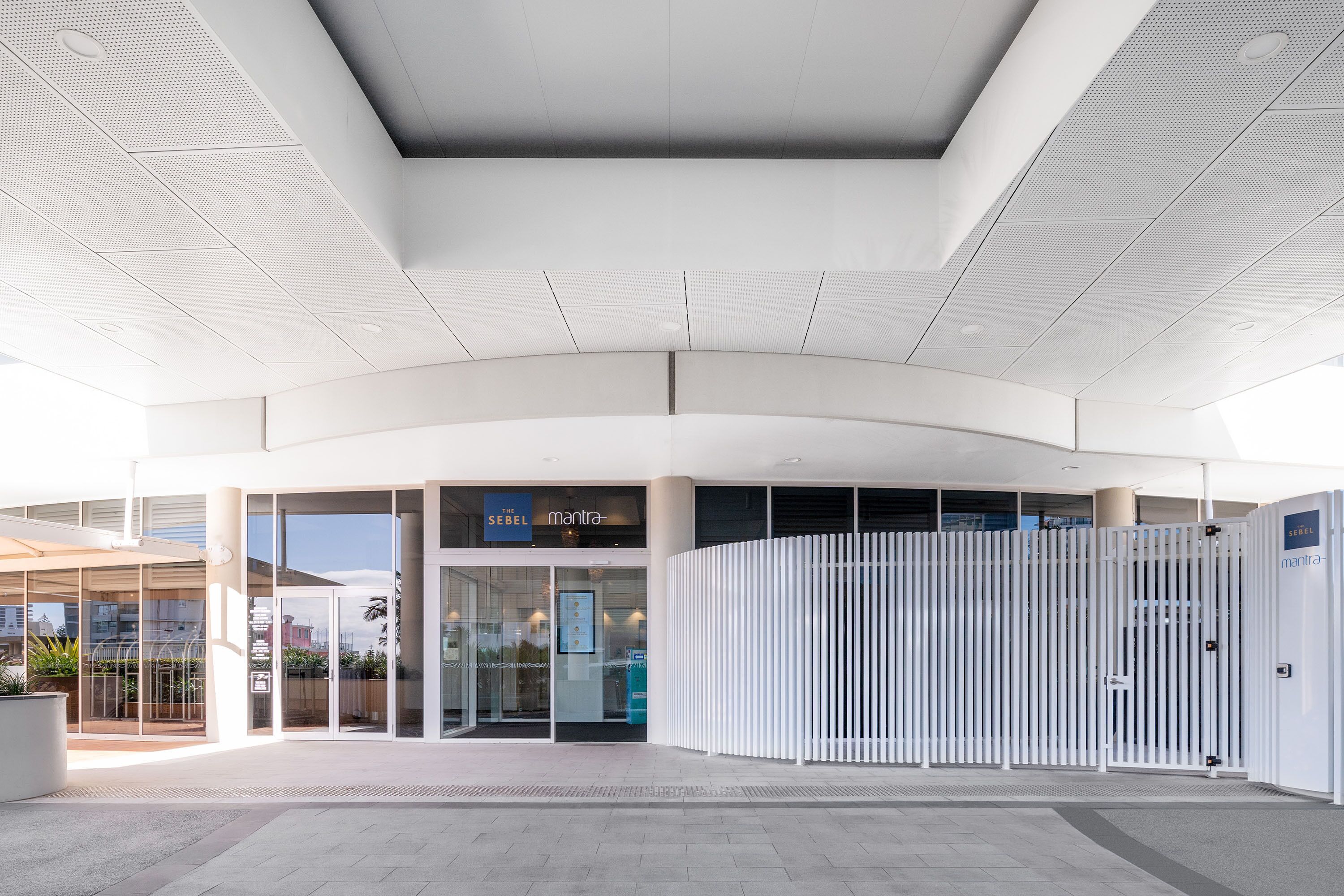 A modern building entrance with glass doors, a sign reading "mantra", and a white fence.