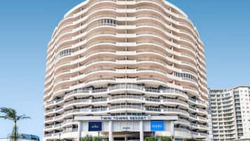 Un hotel de varios pisos con fachada curva, balcones en cada planta y señalización de 'Twin Towns Resort' y 'Mantra+' en la planta baja.