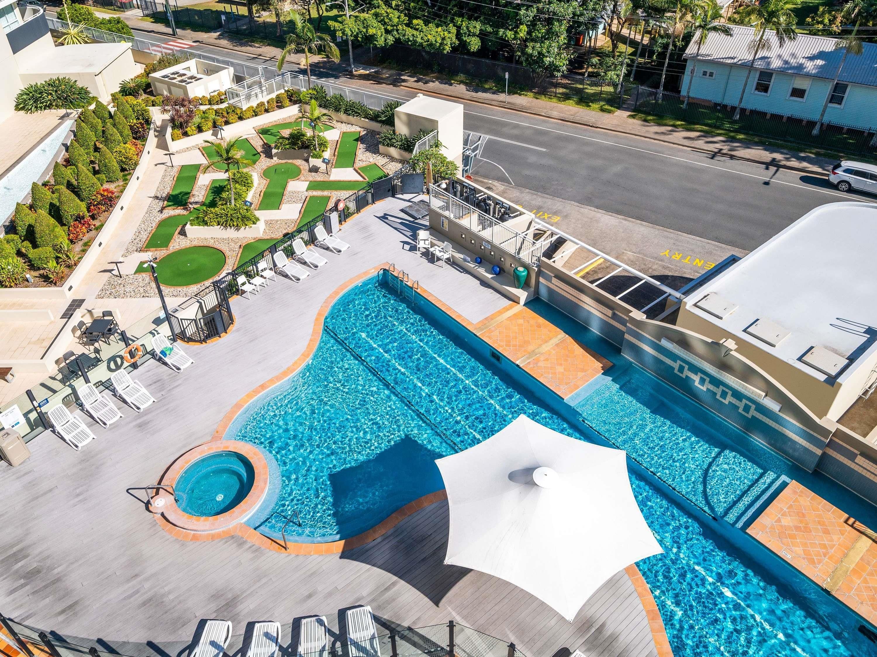 Une piscine dotée d’un parasol, de chaises longues et d’un espace jardin aménagé.
