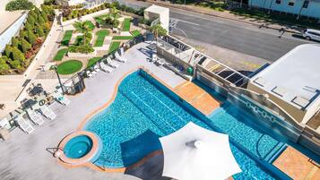 Une piscine dotée d’un parasol, de chaises longues et d’un espace jardin aménagé.