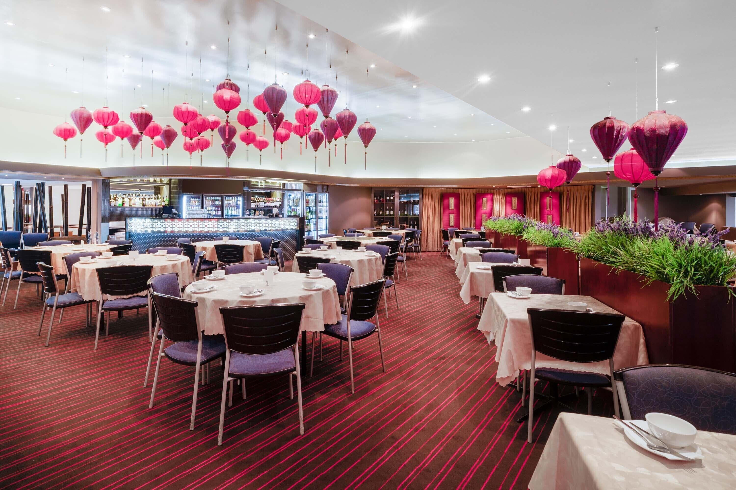 A restaurant with round tables and chairs, red carpet flooring, and hanging red lanterns.