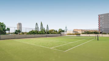 An outdoor tennis court with a net, surrounded by a fence and trees.