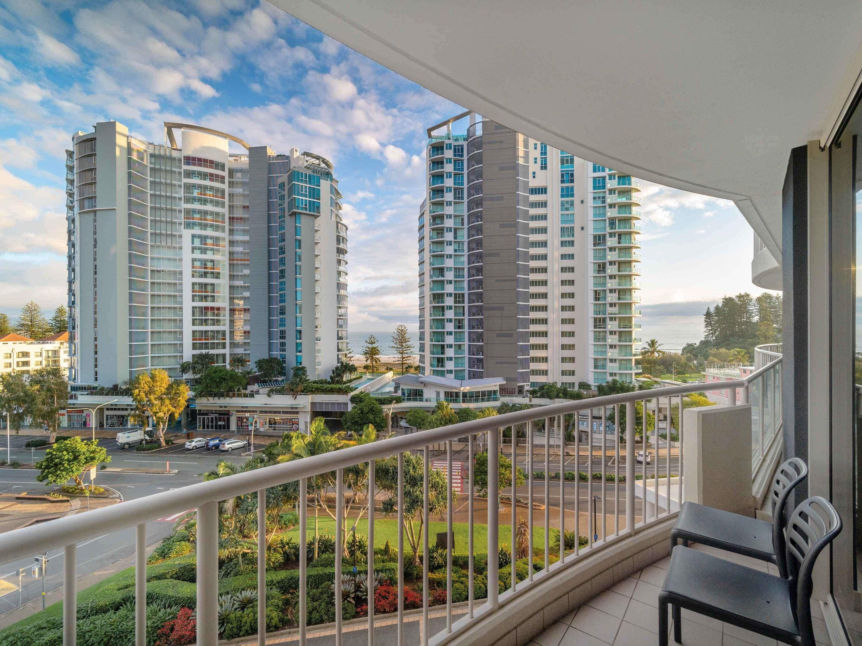 A balcony with a view of high-rise buildings, a road, and greenery.