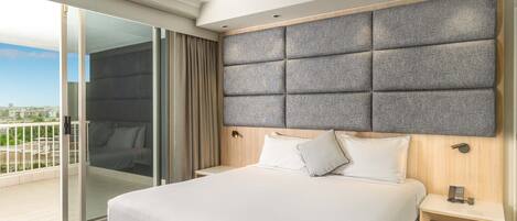 A hotel room with a large bed, a wooden headboard, a bedside table with a phone, and a sliding glass door leading to a balcony.