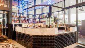 Un espace bar délimité par une paroi de verre, avec des étagères remplies de bouteilles d'alcool et un panneau lumineux au néon.