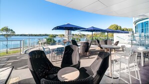 Une terrasse extérieure aménagée avec des meubles en osier, des parasols et offrant une vue sur un plan d’eau.