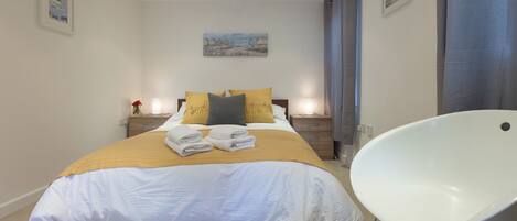 A neatly made bed with a white and yellow duvet, two bedside tables with lamps, and a modern white chair.