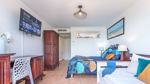 Een slaapkamer met een bed, nachtkastjes, een televisie en een schilderij aan de muur.