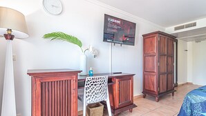 Hotelkamer met een houten bureau, een stoel, een aan de muur bevestigde televisie, een klok en een kledingkast.
