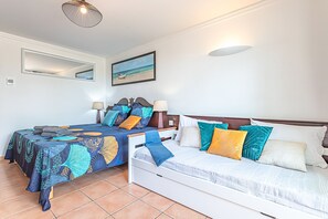 Een slaapkamer met twee bedden, een grote spiegel en een schilderij met een strandthema.