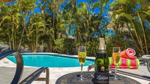 Escena junto a la piscina con una botella de champán, dos copas y una toalla.