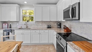 Una cocina moderna con armarios blancos, encimera de granito, microondas integrado y cafetera.