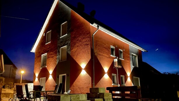 A two-story building with a red and black facade, illuminated by exterior lights. - Beautiful vacation apartment at the pulse of the Green Hell (Kelberg)