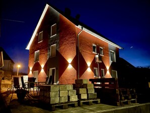 Un edificio de dos pisos con fachada roja y negra, iluminado por luces exteriores.
