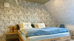 A bedroom with a sloped ceiling, a wooden bed frame, a nightstand, and a wall-mounted thermostat. - Beautiful vacation apartment at the pulse of the Green Hell (Kelberg)