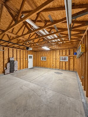 A spacious indoor area with a high ceiling and wooden beams, featuring a concrete floor and a white door. - Walk to Lucas Oil Stadium - Clean 4BR Home (Indianapolis)
