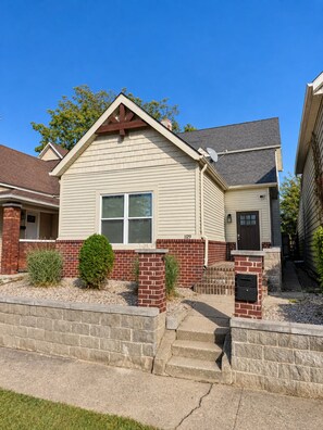 A single-story house with a gabled roof, a front porch, and a brick foundation. - Walk to Lucas Oil Stadium - Clean 4BR Home (Indianapolis)