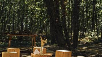Relax on the deck surrounded by tall trees, with a woven table and comfortable stools.