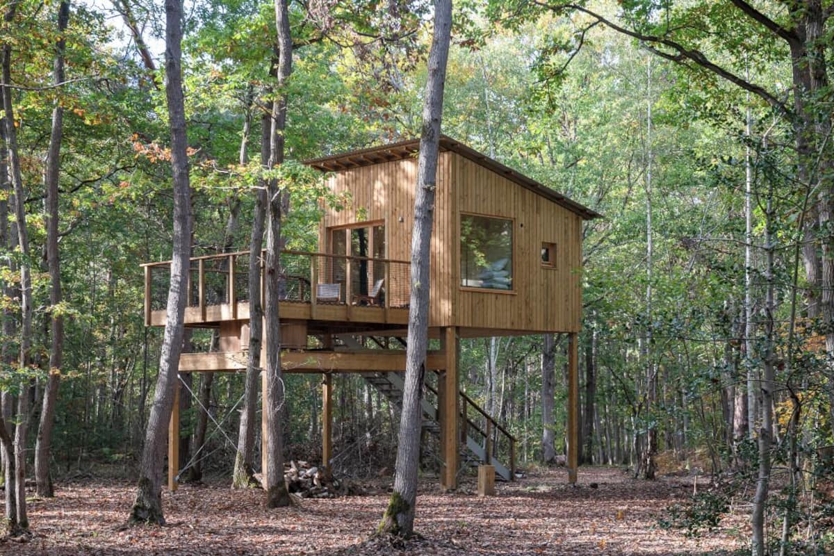 Een houten boomhut met een balkon, omringd door een bos.