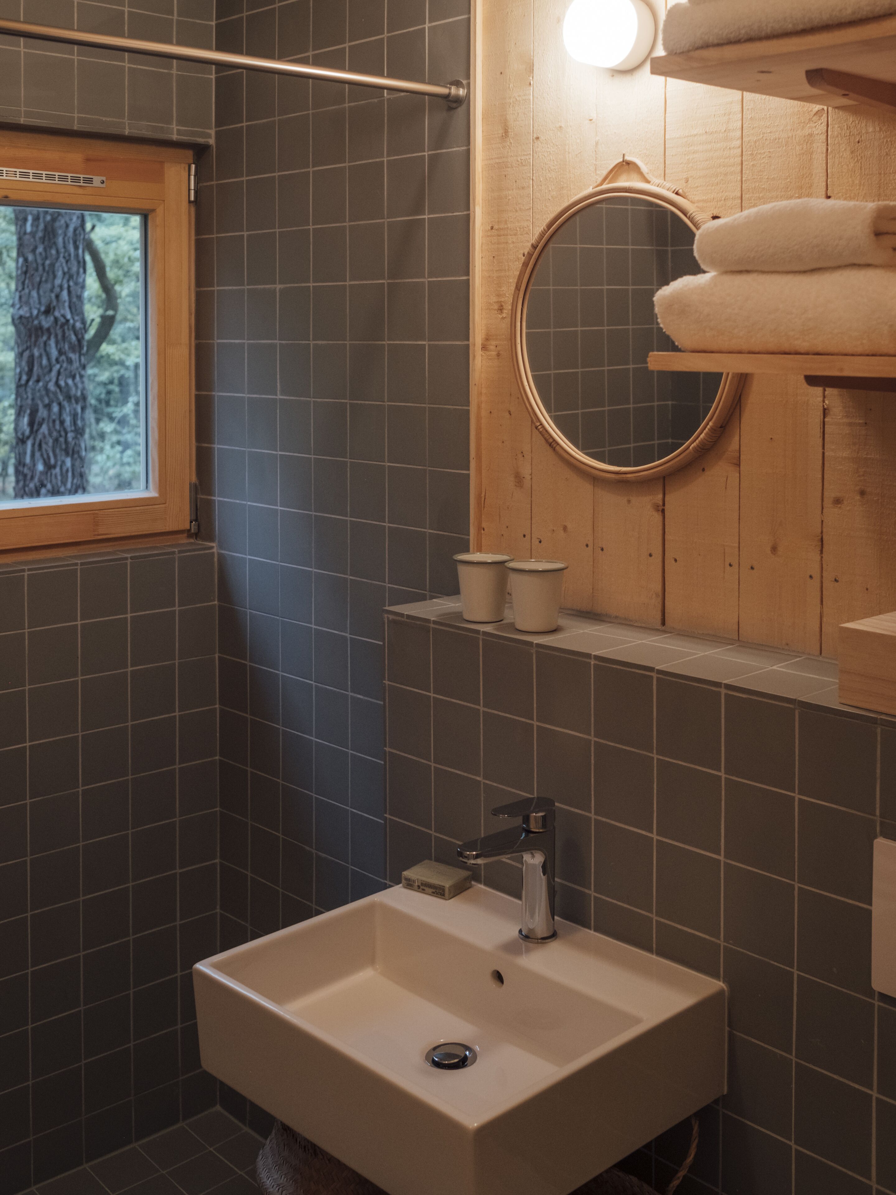 Un baño con ventana, lavamanos, espejo y perchero para toallas.