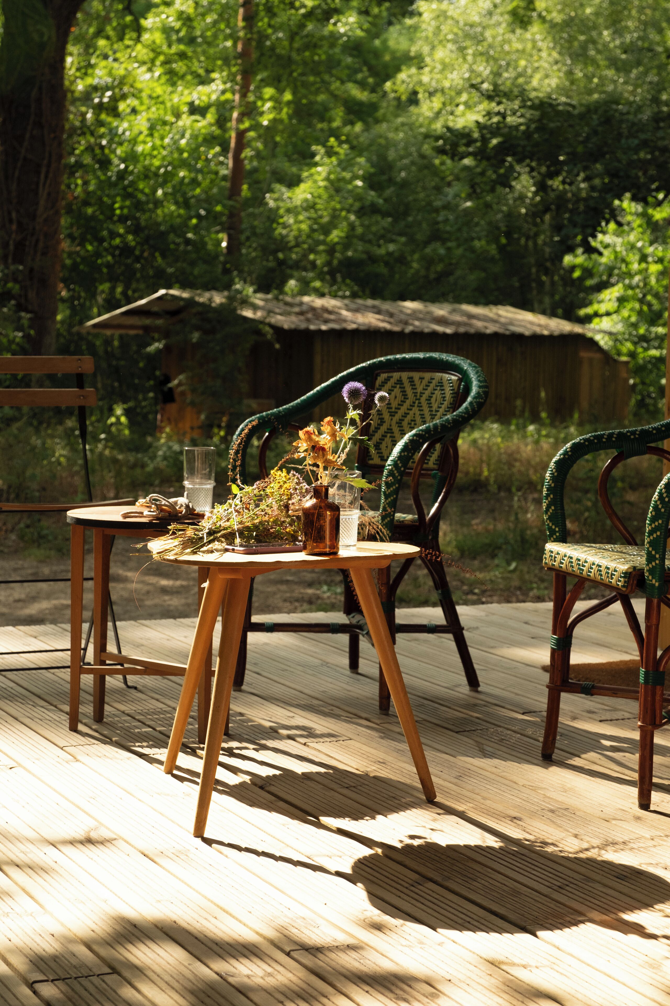Eine Holzterrasse mit zwei Korbstühlen und einem kleinen Tisch, umgeben von üppiger Bepflanzung.