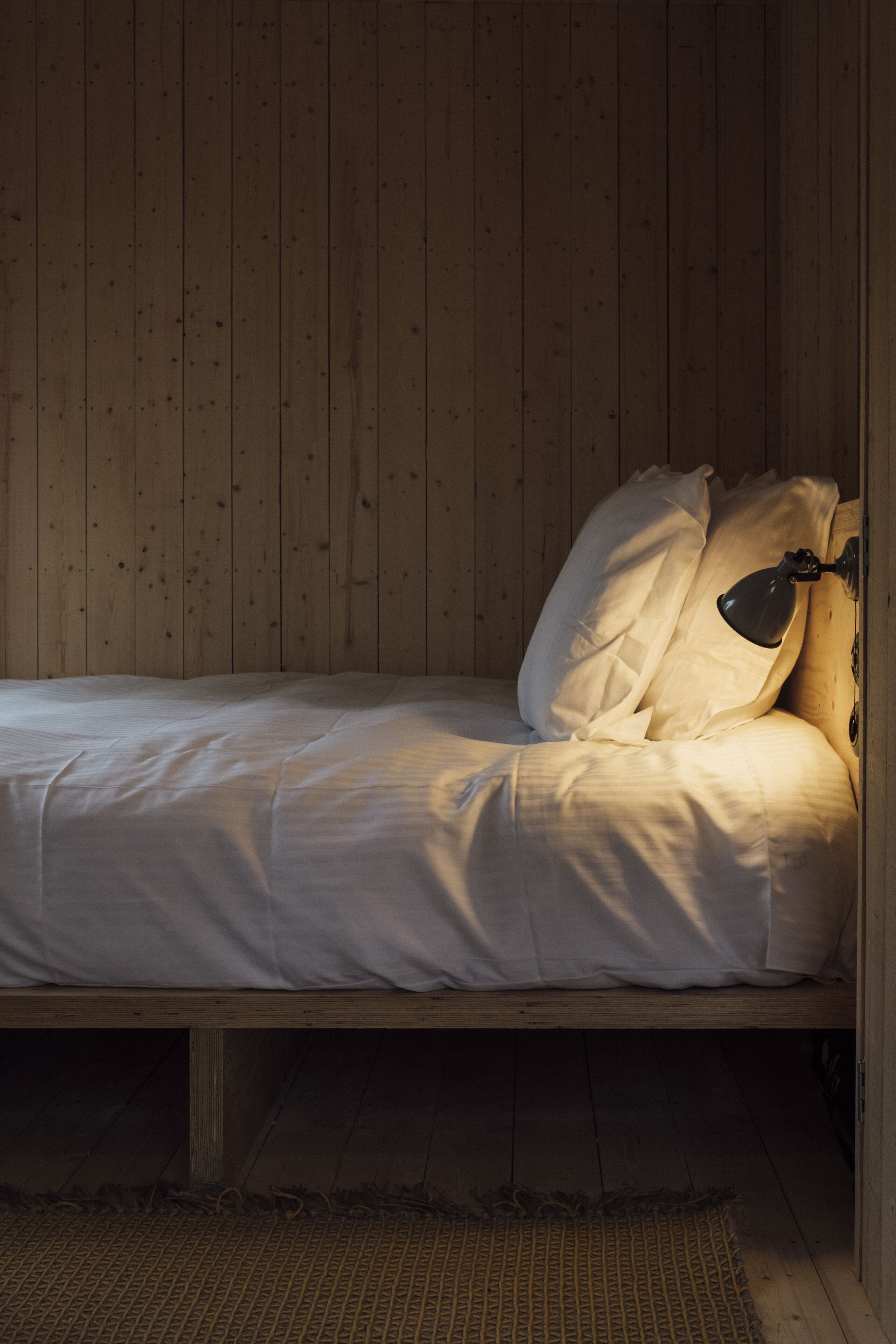 Una cama pequeña y acogedora con cabecera de madera y una l ámpara de noche.