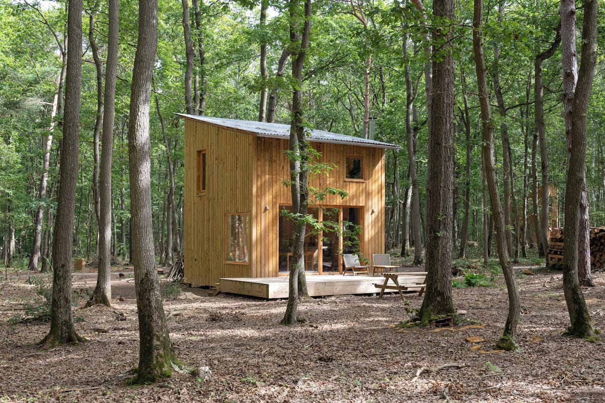 Een houten chalet in een bos, met een veranda en zitgedeelte.