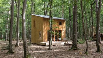 Une cabane en bois située dans une forêt, avec une véranda et un espace salon.