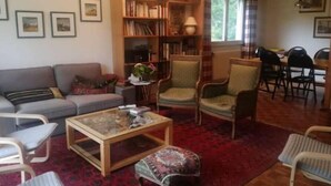 A cozy living room with a sofa, armchairs, a coffee table, a bookshelf, and a dining area with chairs. - Maison Familiale "les 3 Roches" (Xonrupt-Longemer)
