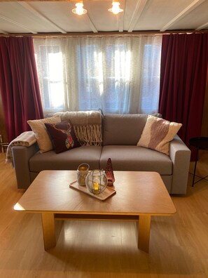 A living room with a sofa, a coffee table, and a window with curtains.