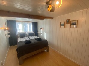 A bedroom with a wooden bed, two bedside tables, a window with curtains, and wall-mounted lights.
