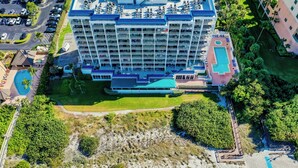 A multi-story hotel with a pool area, surrounded by greenery and a beach. - Beachfront Living at the Apollo I On-Site Sunset Grille Tiki/Restaurant (Marco Island)