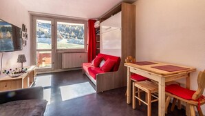 Ein gemütliches Zimmer mit einem Holztisch und Stühlen, einem roten Sofa und einem großen Fenster mit Blick auf eine verschneite Landschaft.